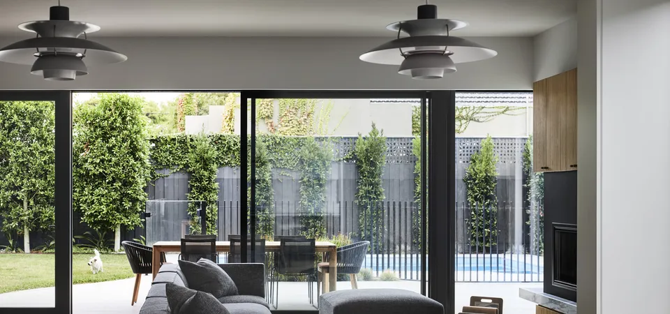 Open-plan living area with grey sofa, pendant lights and large sliding doors opening to pool garden