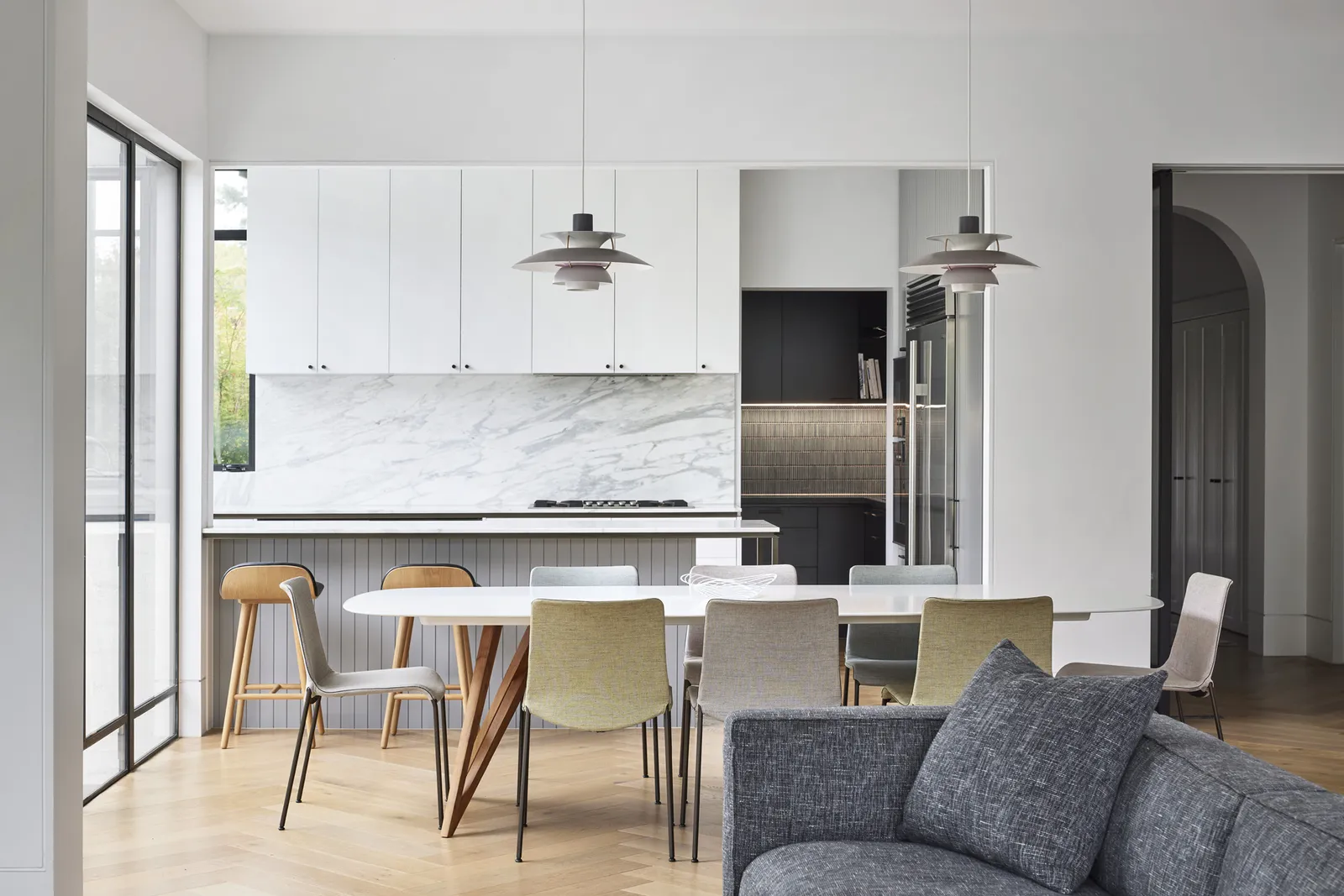 Open-plan kitchen and dining with marble splashback, white cabinetry and pendant lights over dining table