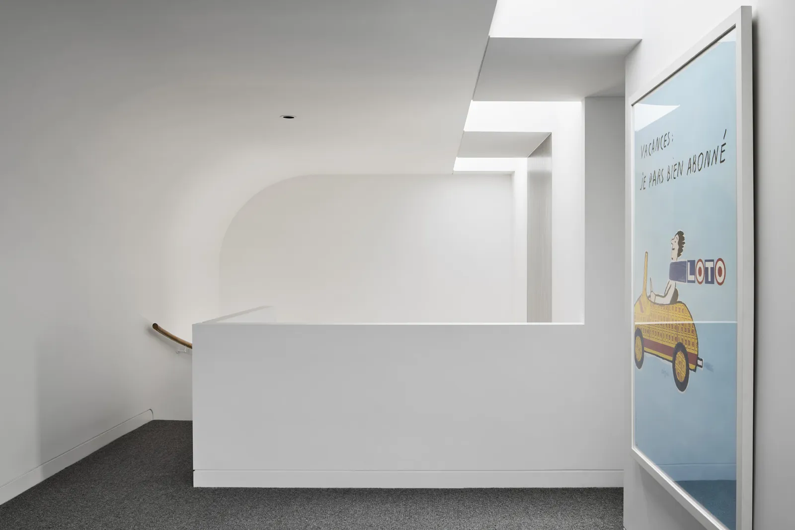 Minimalist white stairwell landing with curved wall detail and vintage Loto poster artwork